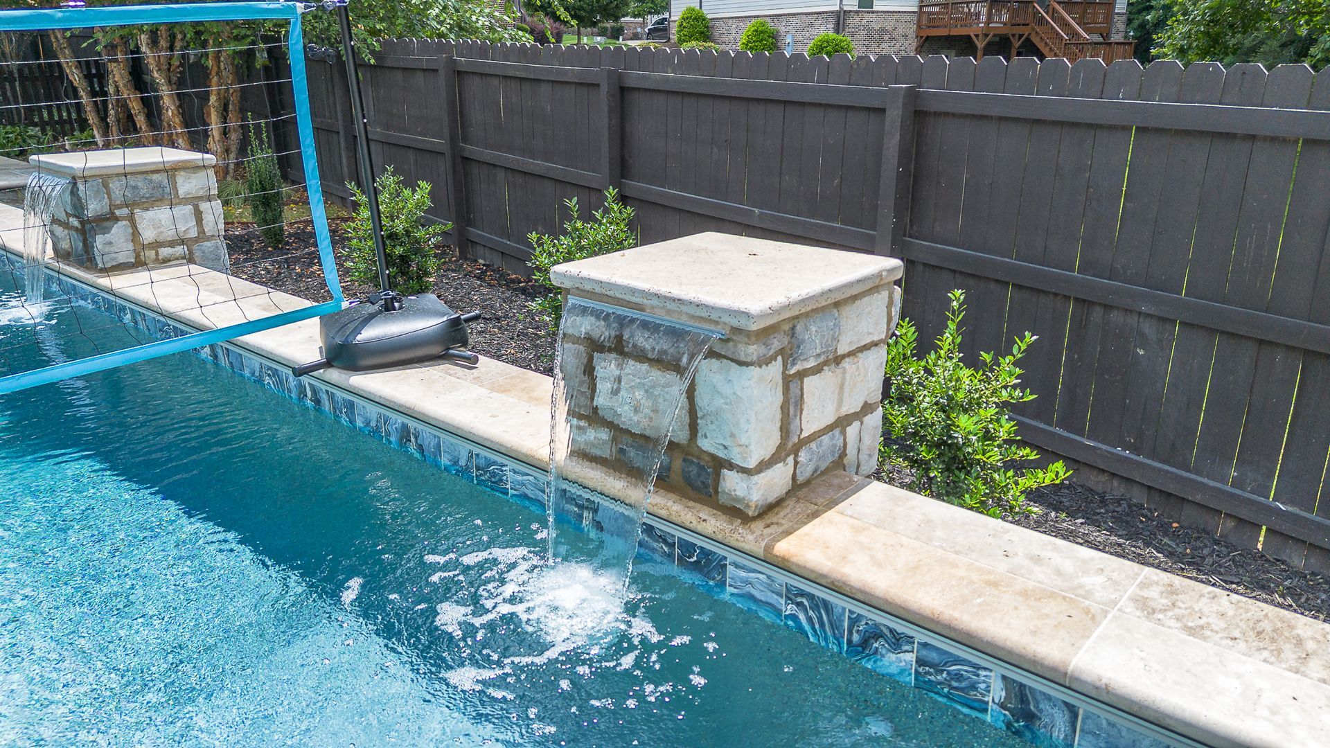 Swimming pool with stone pillars, dark fence, and blue water.