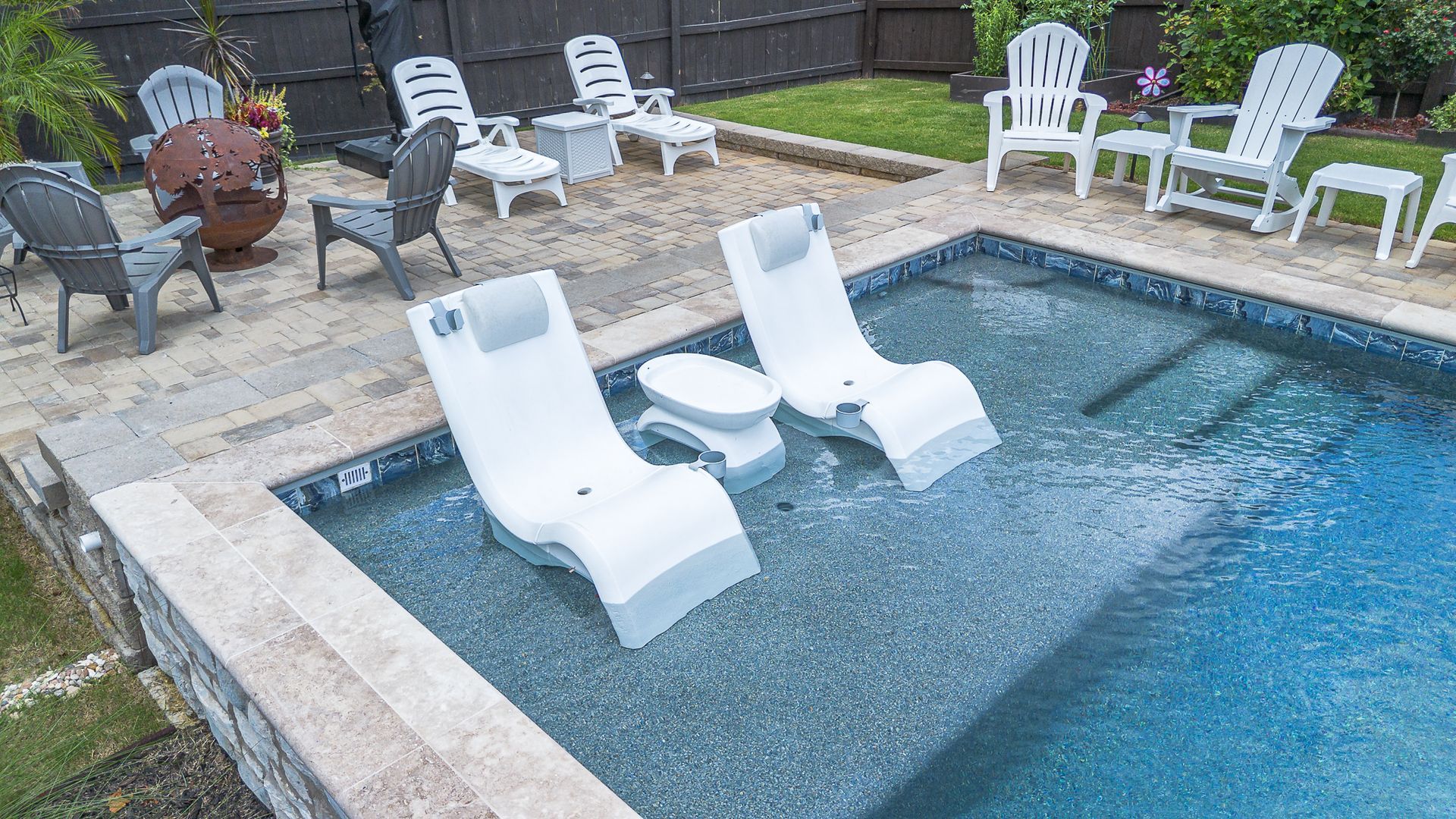 Small pool with white lounge chairs, patio furniture, and green grass.