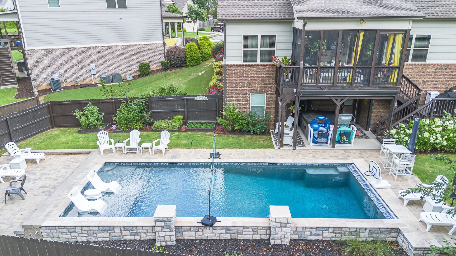 Backyard with a pool, lounge chairs, and a two-story house with a screened-in porch.