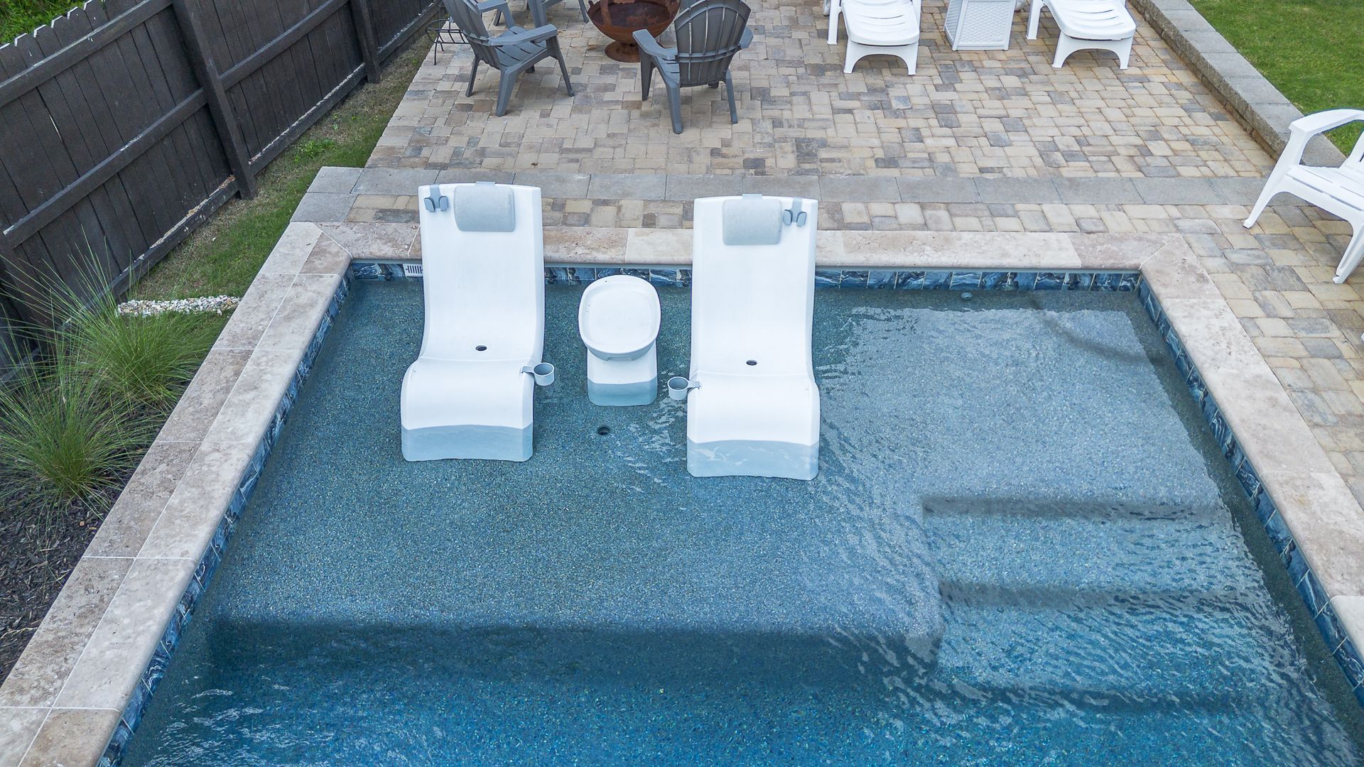 Swimming pool with two white lounge chairs and a small table.