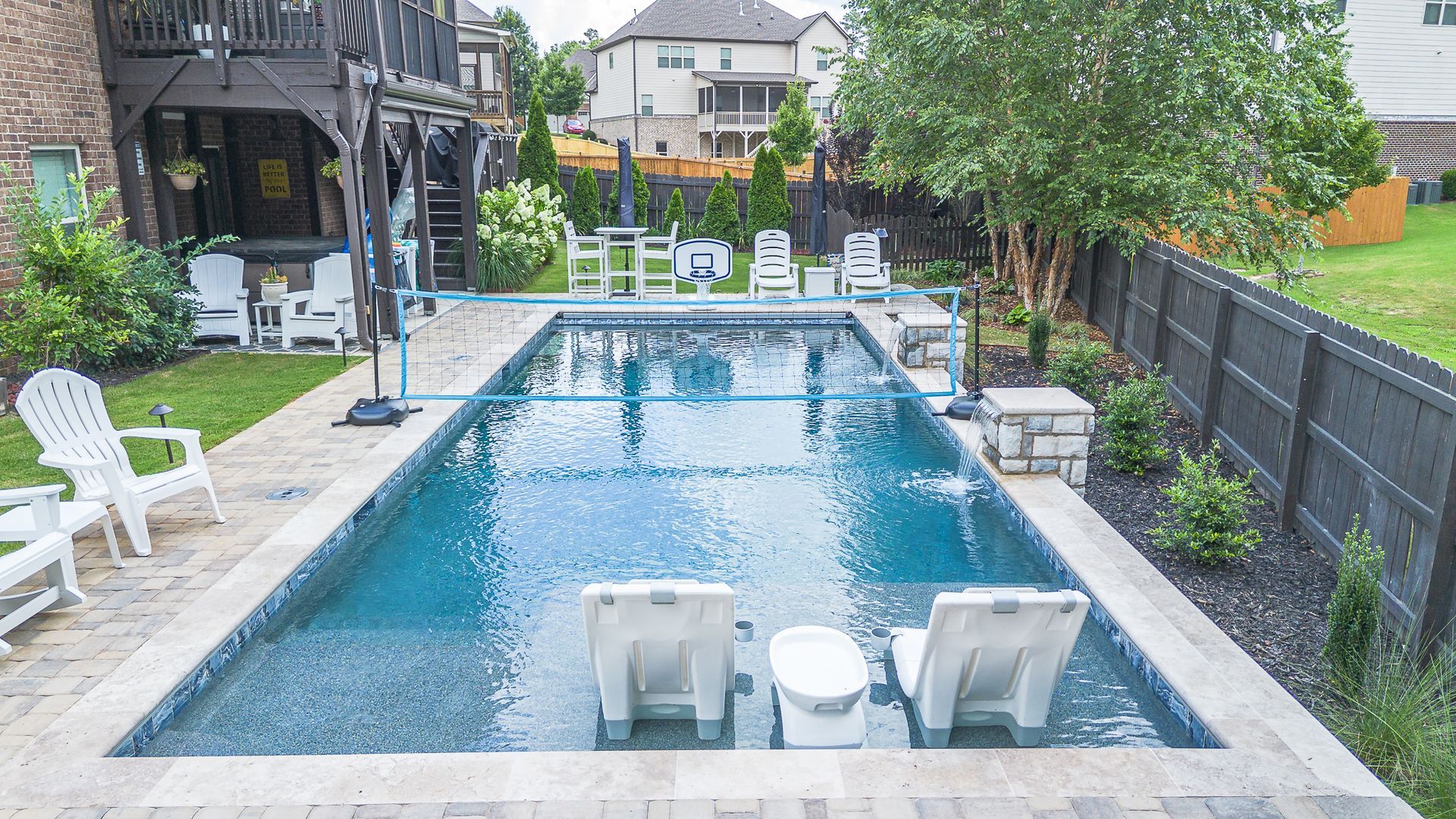 Backyard pool with lounge chairs, surrounded by beige stone and landscaping.