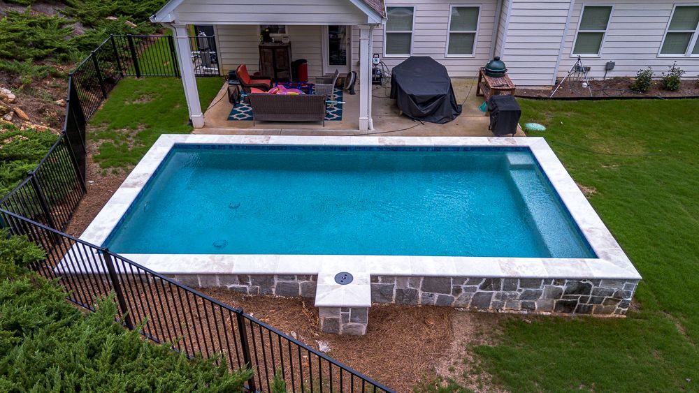 Rectangular backyard pool with blue water, stone walls, and a covered patio.