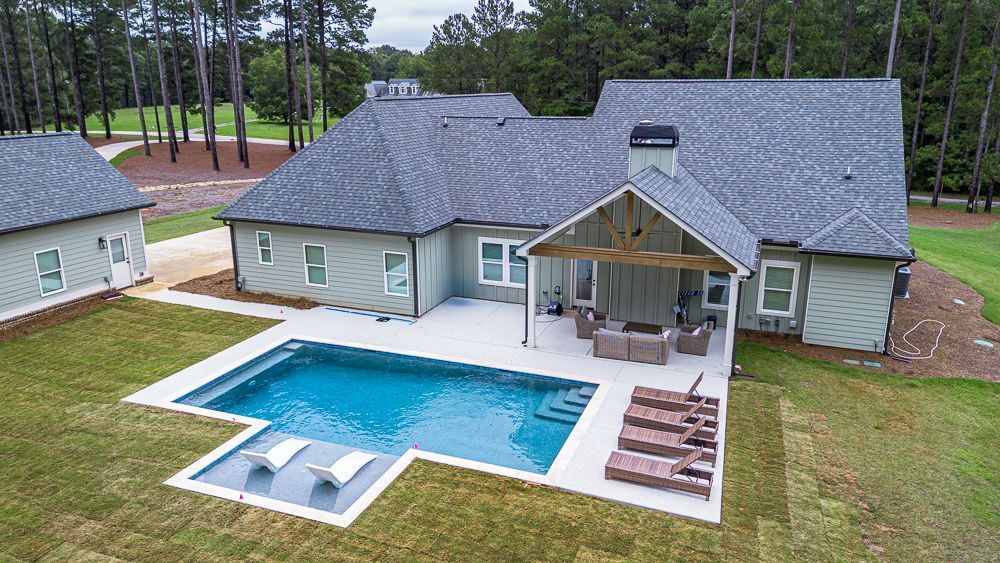 A light green house with a pool and outdoor seating on a grassy lawn.