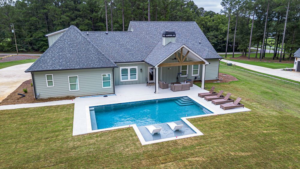 Backyard with a pool, patio, and house. The pool is blue; the house is green, and the patio is concrete.