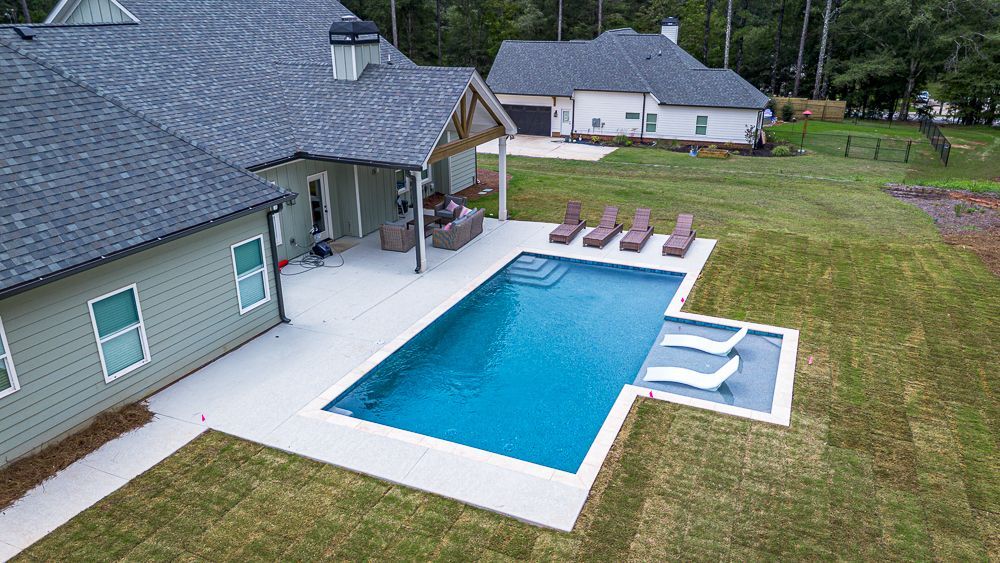 Backyard with a pool, patio, and house; green grass, blue water.
