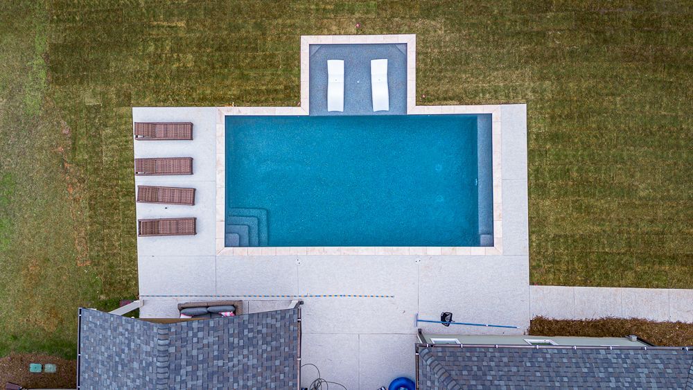 Overhead view of a rectangular swimming pool with lounge chairs and a grassy yard.