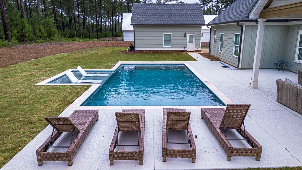 A rectangular pool with lounge chairs on a patio, small houses in the background.