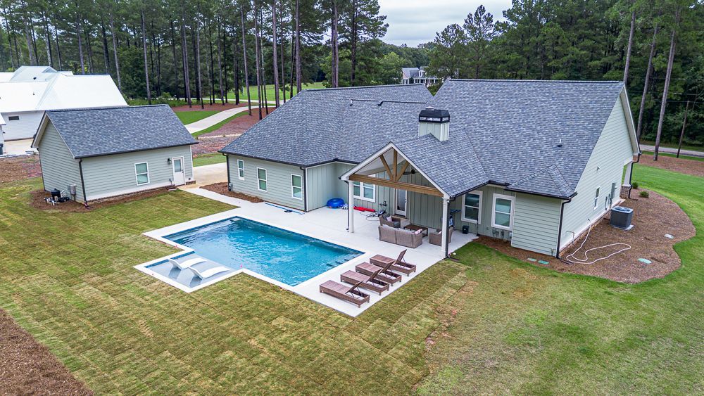 Backyard of a house with a pool, seating, and a shed. Light green house with a dark gray roof.