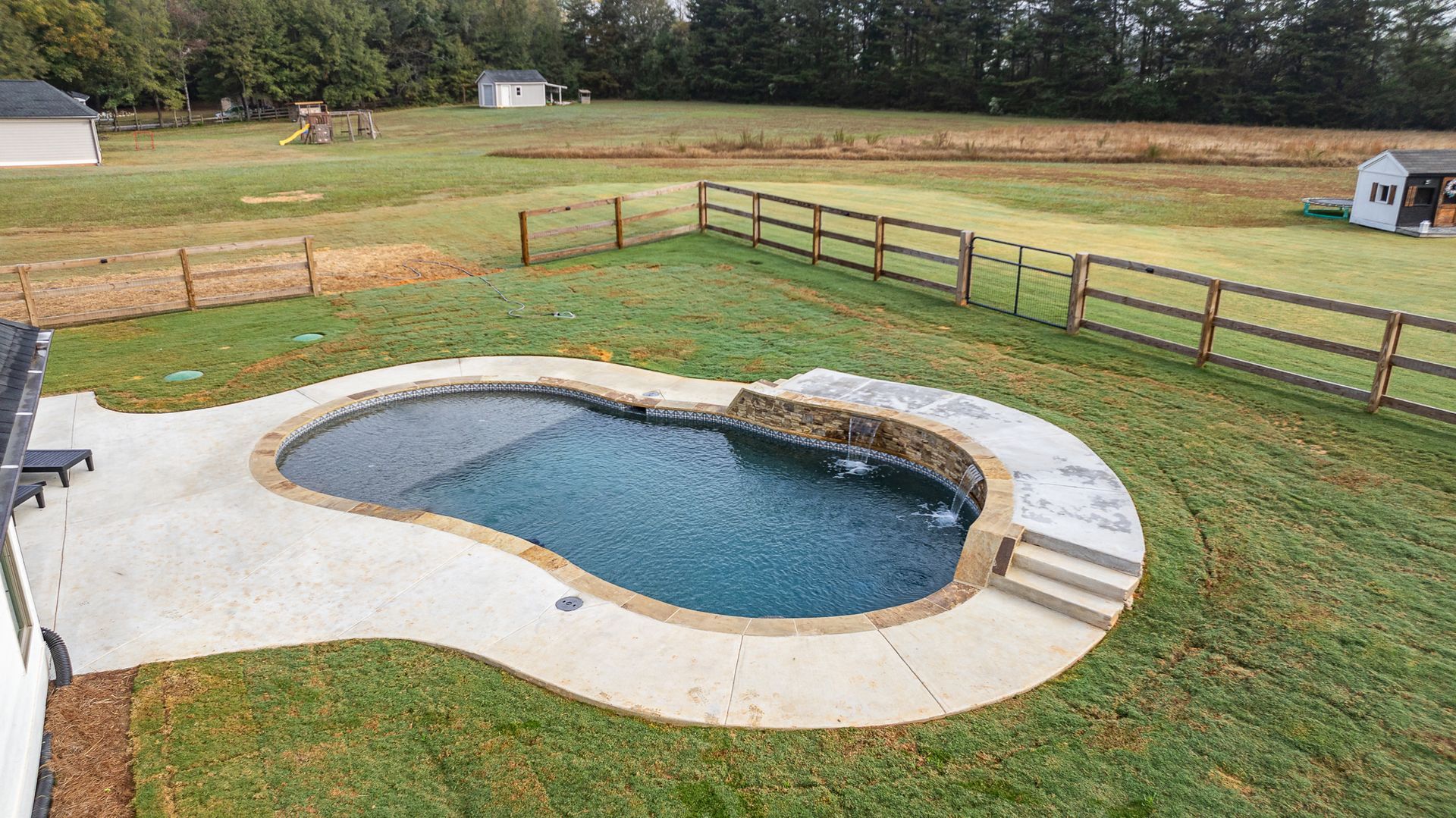 There is a large swimming pool in the middle of a lush green field.