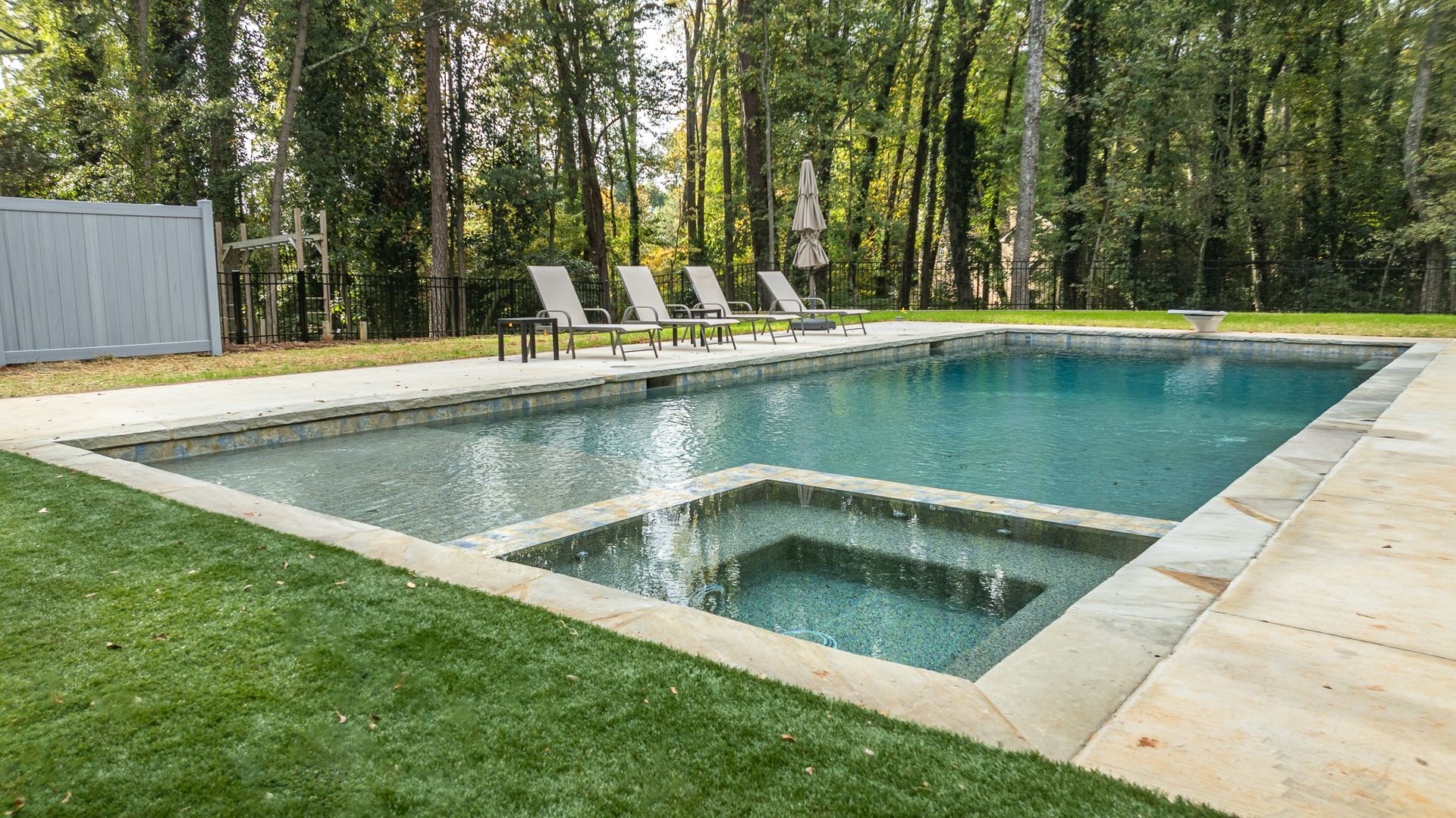 A large swimming pool surrounded by chairs and trees in a backyard.