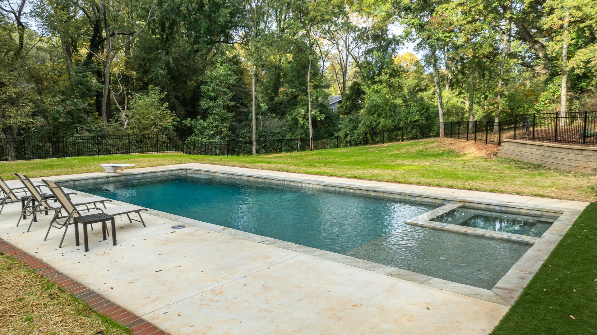 A large swimming pool surrounded by chairs and trees in a backyard.