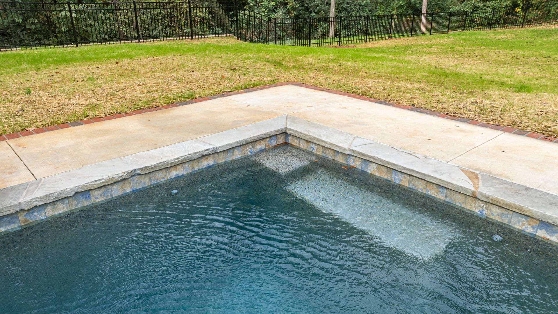 A swimming pool with a concrete border and a fence in the background.