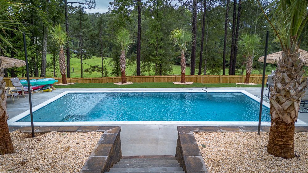 Rectangular pool with turquoise water, palm trees, and steps leading to it in a backyard setting.