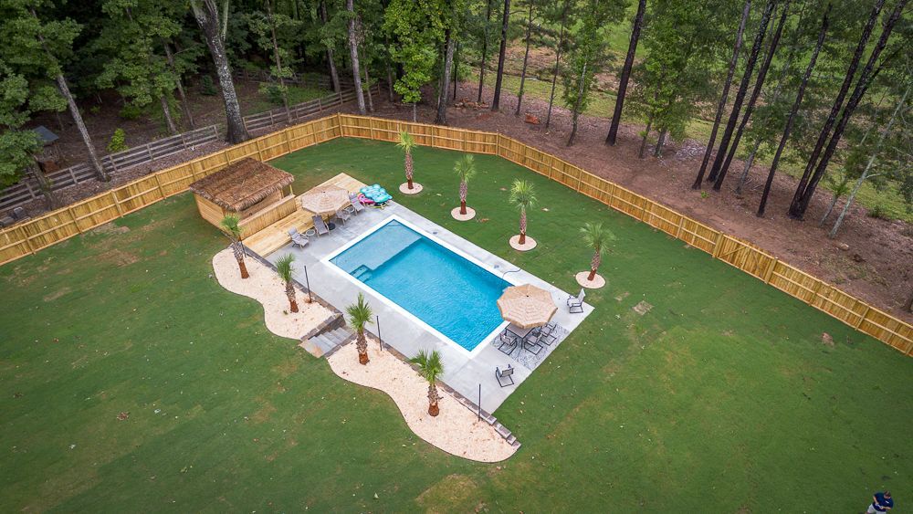 Aerial view of a rectangular pool in a backyard, surrounded by a fence and palm trees.