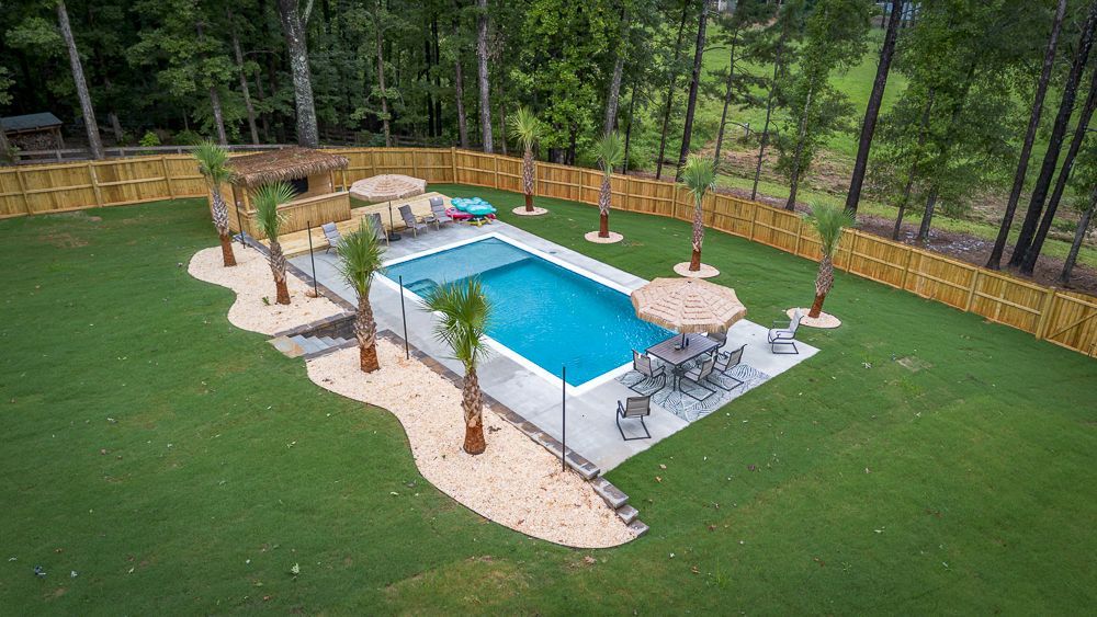 Aerial view of a backyard with a rectangular pool, surrounded by a fence and palm trees.