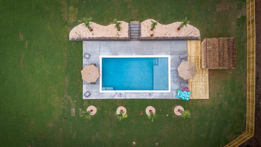 Overhead view of a pool with a small cabana, and landscaping on green grass.