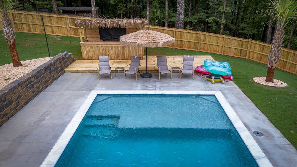 Swimming pool with lounge chairs, tiki bar, and green lawn.
