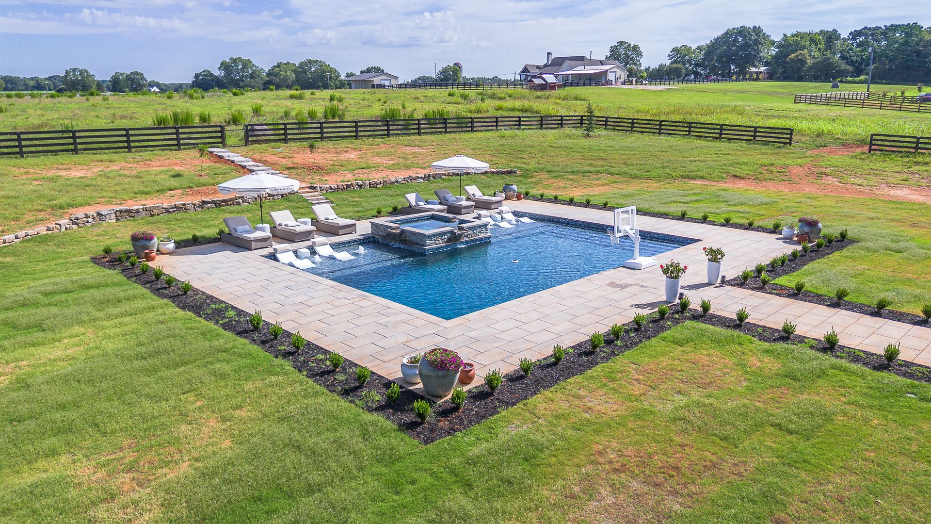 Outdoor swimming pool with lounge chairs, surrounded by green grass and countryside.