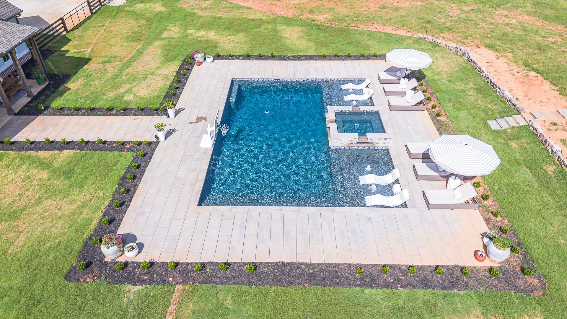 Aerial view of a backyard pool with lounge chairs and umbrellas on a manicured lawn.