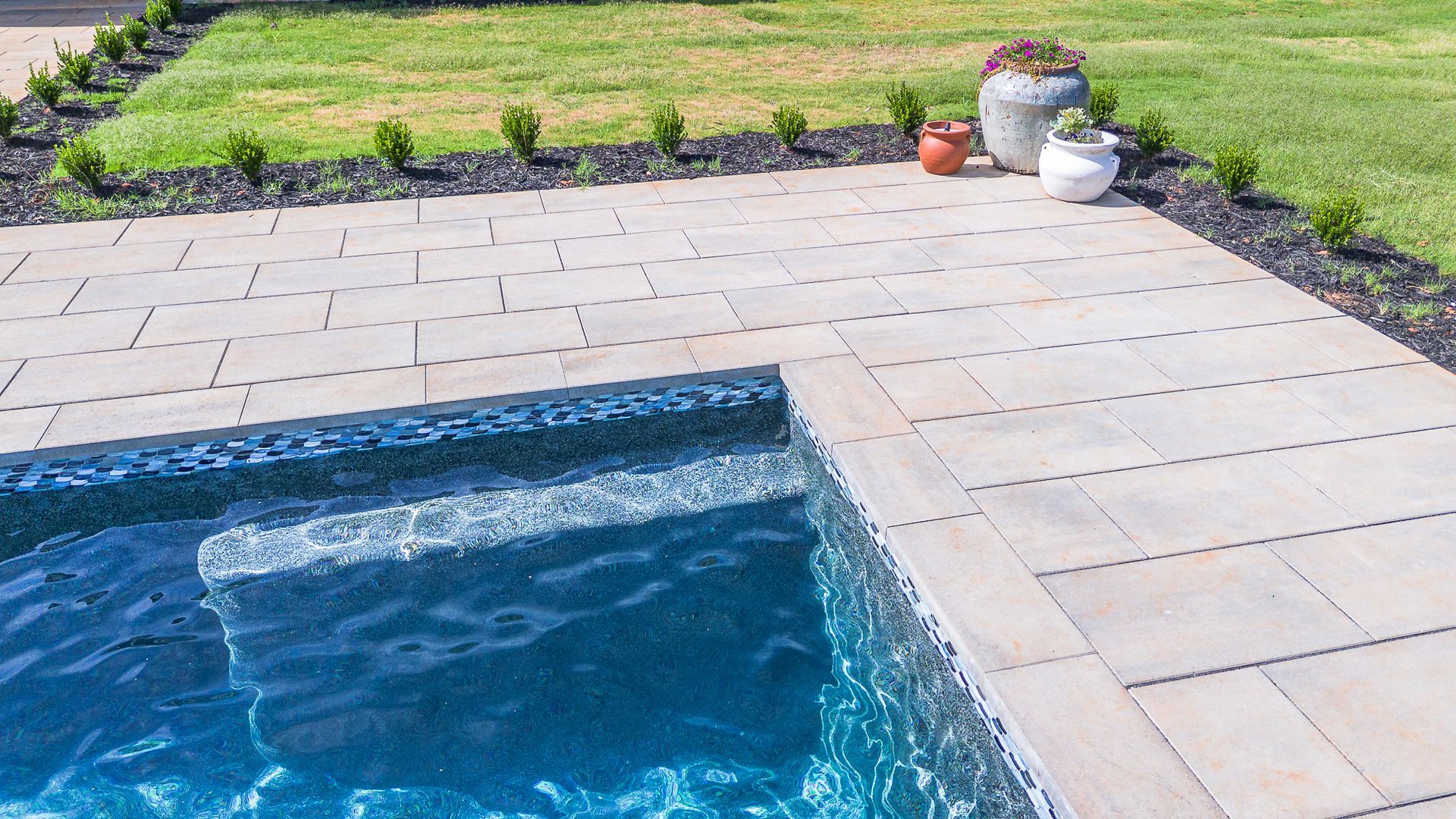 Pool with steps and patio, surrounded by grass and landscaping.