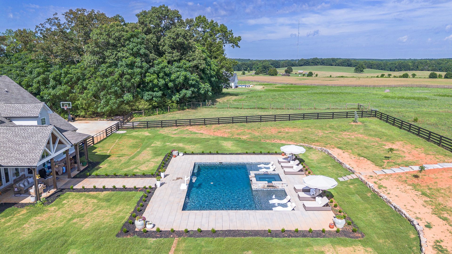 Aerial view of a house with a pool, surrounded by green grass, next to a farm field.