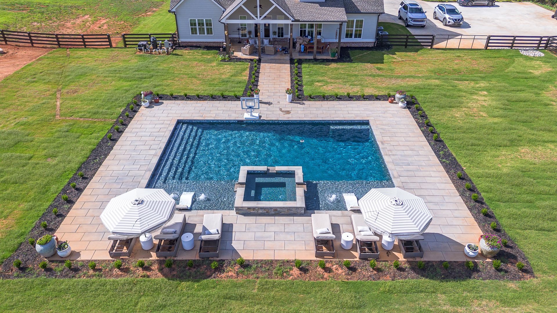 Aerial view of a luxury home with a rectangular pool, lounge chairs, and umbrellas.