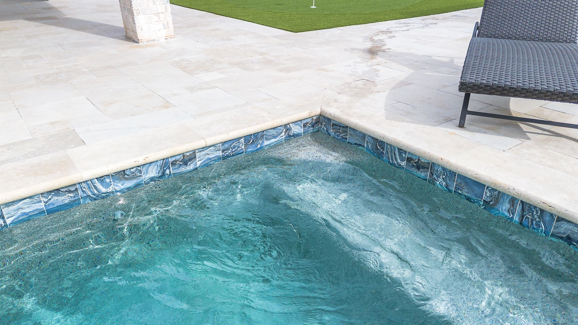 Pool with turquoise water, tiled edge, and a chair on a deck.