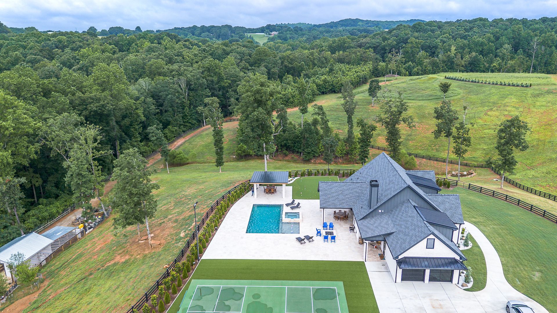 Luxury house with pool and tennis court, surrounded by trees and rolling hills.