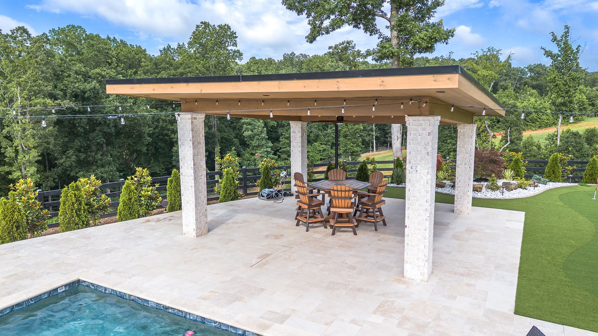 Patio with a table and chairs, surrounded by white pillars and green grass, near a pool.
