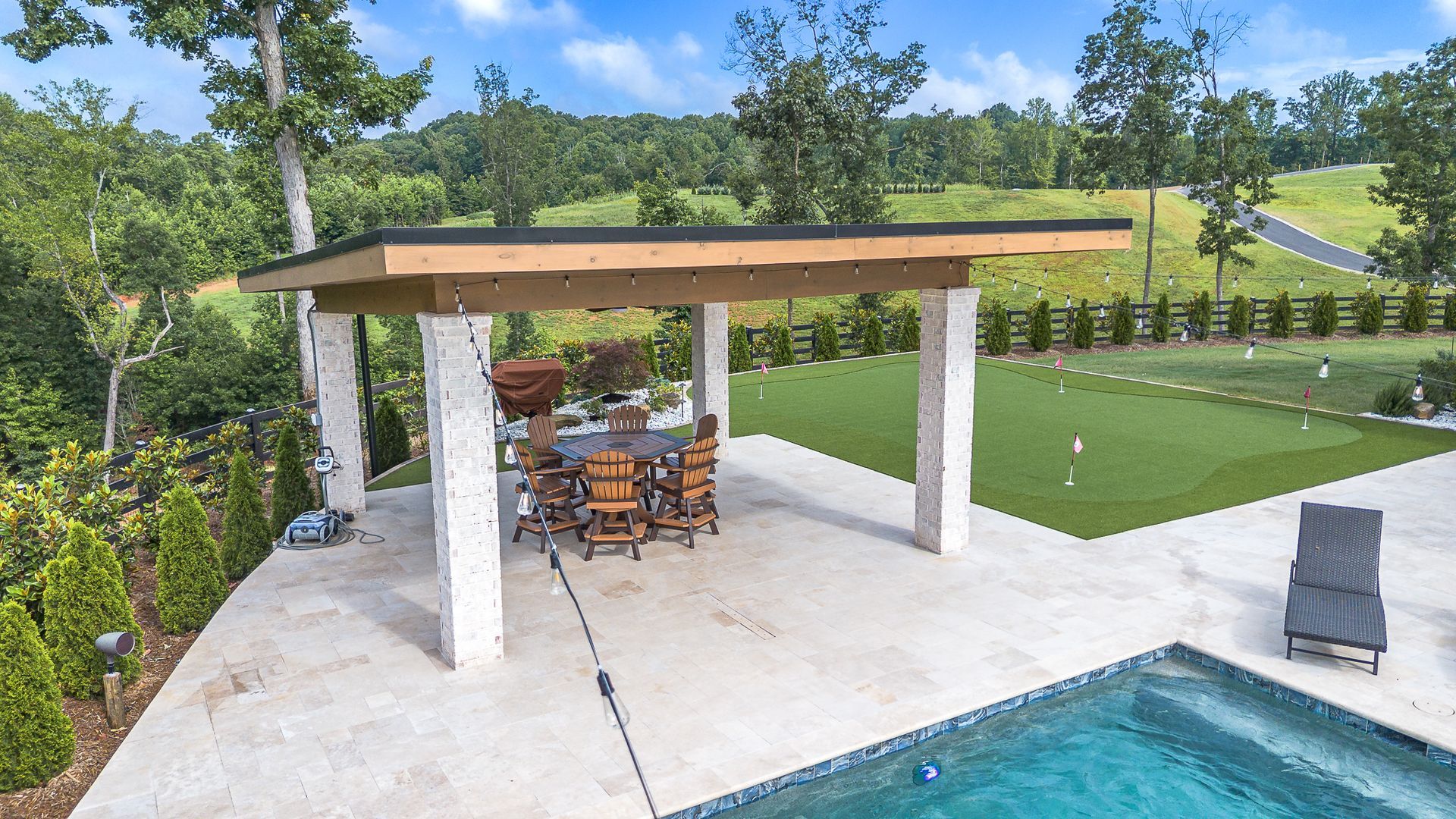 Outdoor dining area with a pool, golf green, and rolling hills in the background.