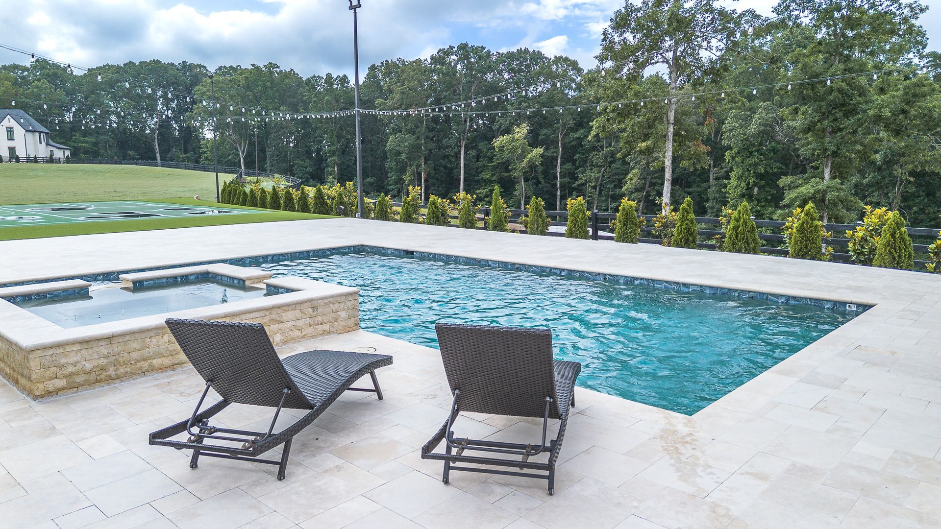 Swimming pool with two lounge chairs, hot tub, trees in background.