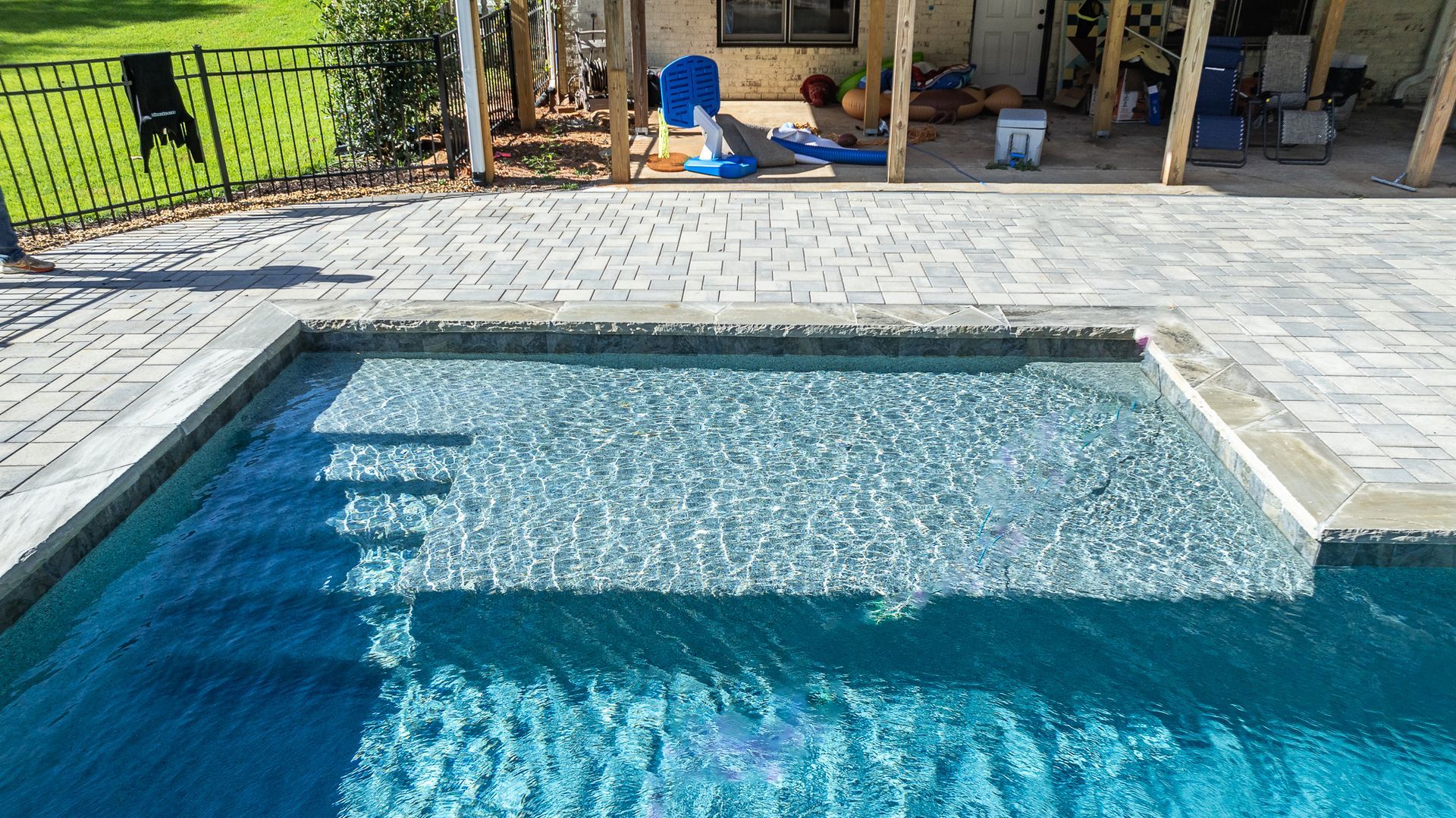 A large swimming pool with stairs leading to it is surrounded by a brick patio.