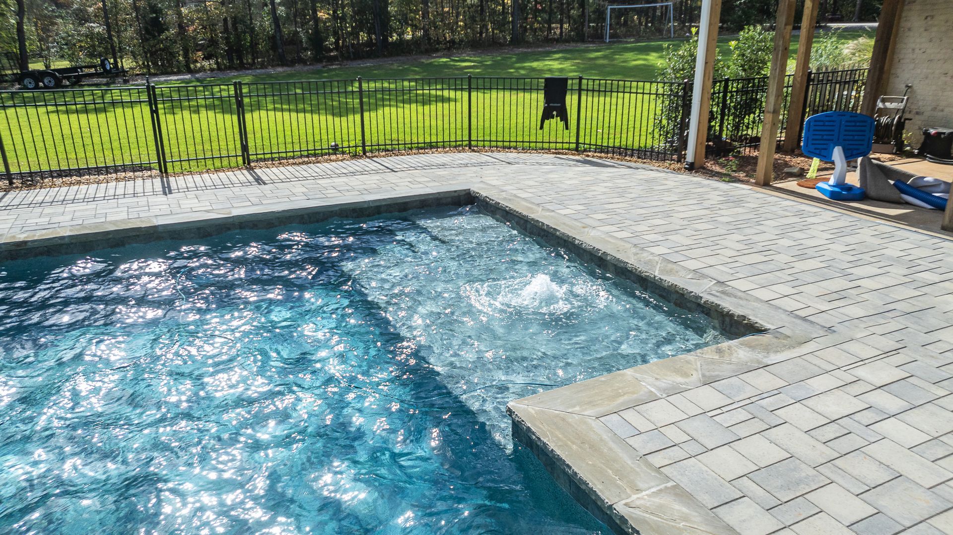 A large swimming pool is surrounded by a fence and a patio.