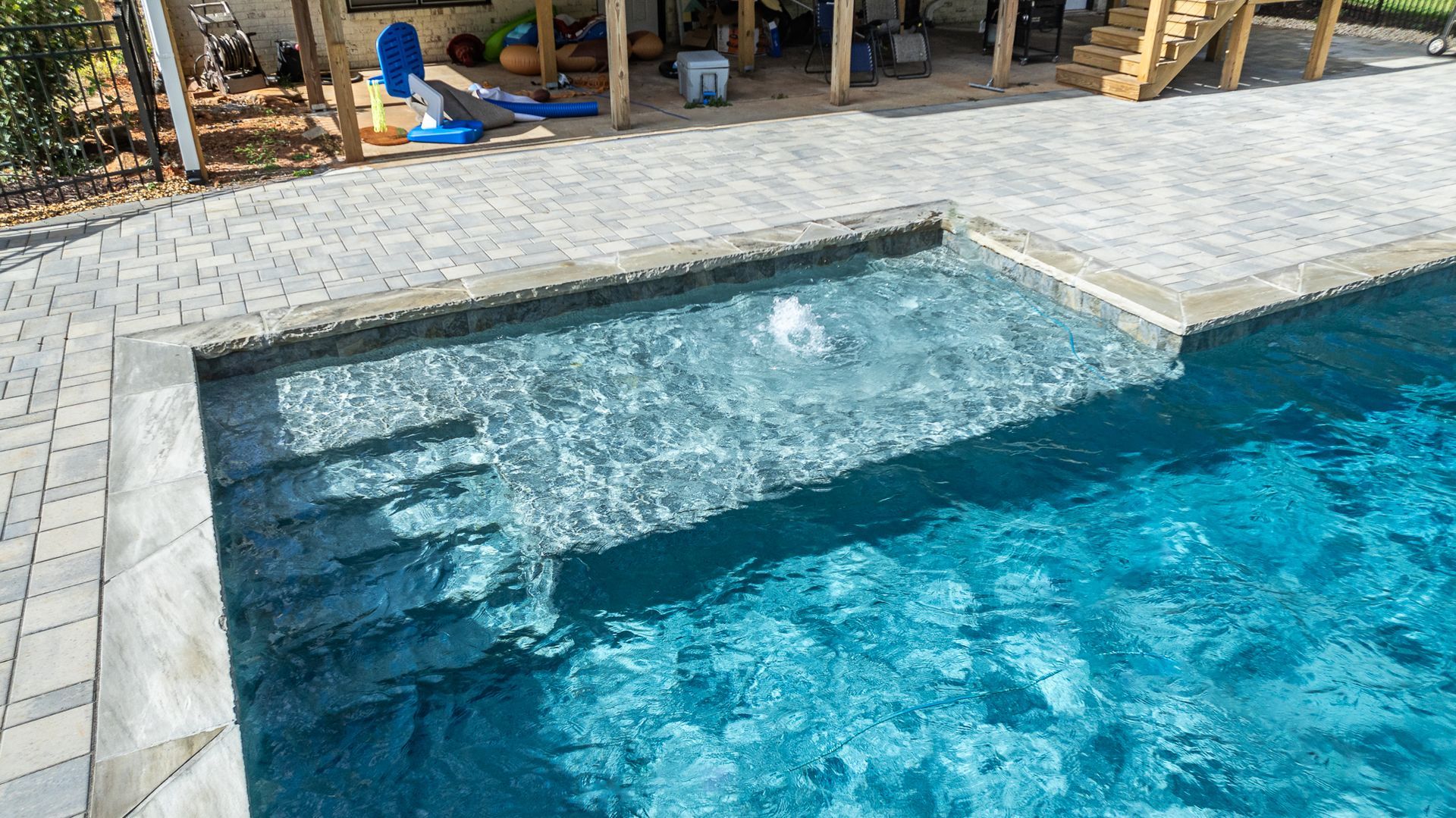 A swimming pool with stairs leading to it and a patio in the background.