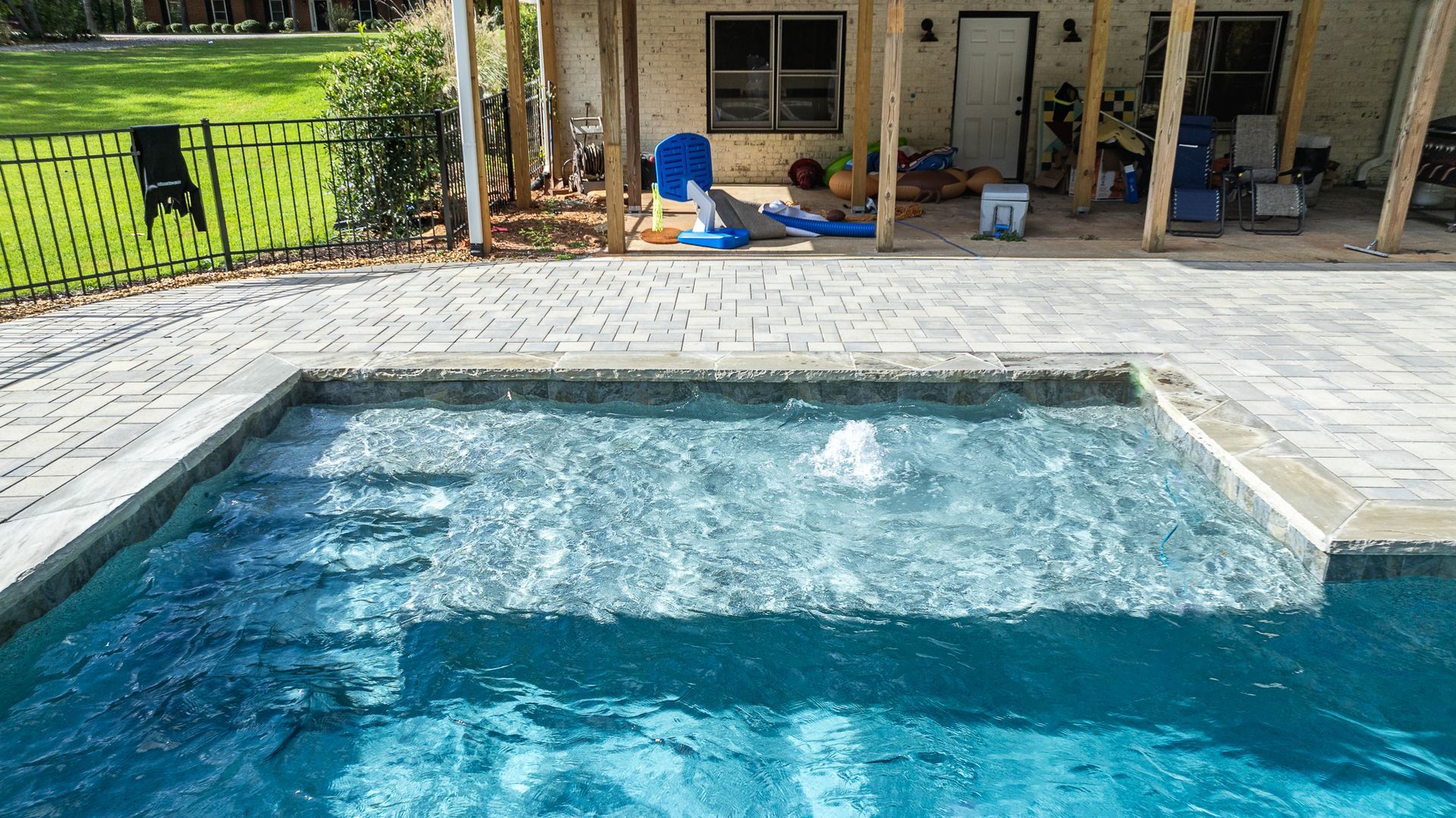 A large swimming pool is sitting on top of a brick patio next to a house.