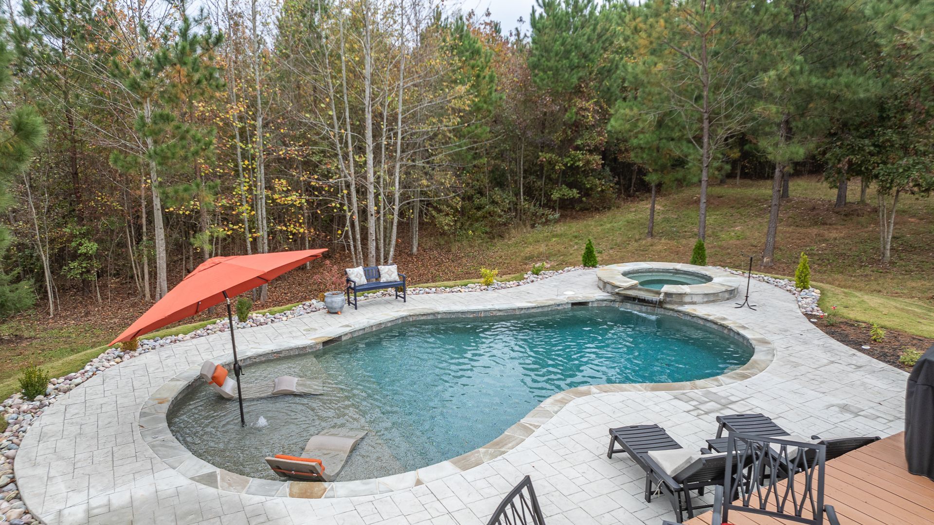 A large swimming pool with a red umbrella in the middle of it surrounded by trees.