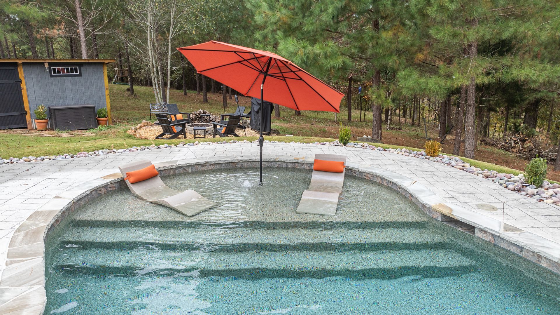 A swimming pool with a red umbrella and two lounge chairs in it.