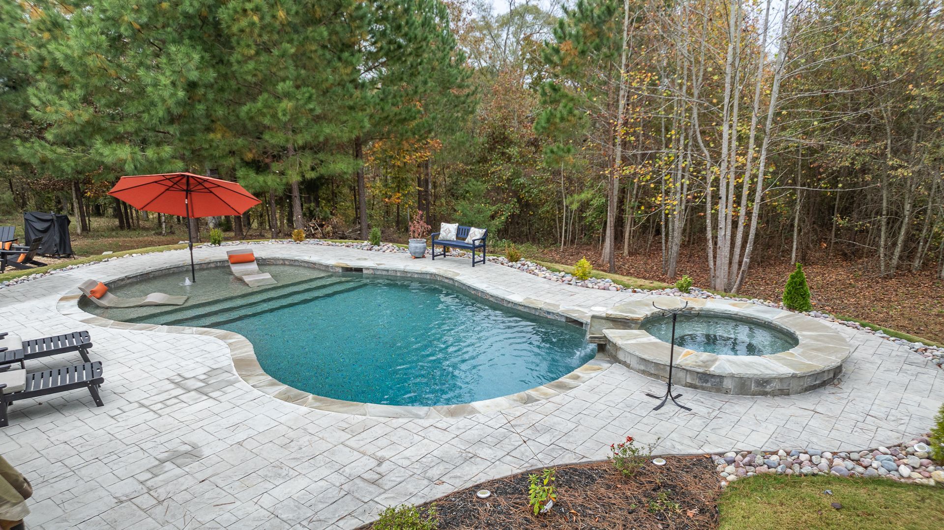 A large swimming pool with a hot tub and an umbrella in the backyard.