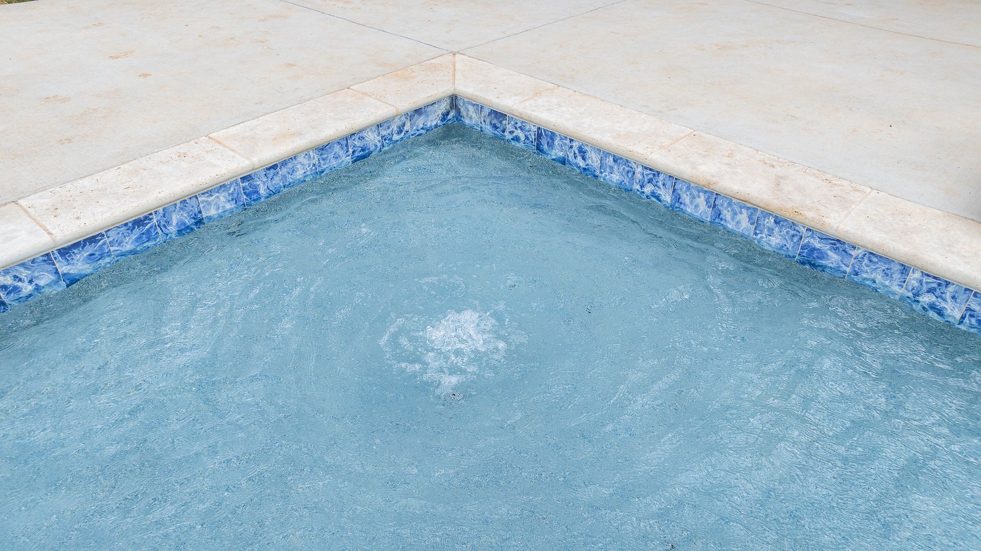 A close up of the corner of a swimming pool with blue tiles.