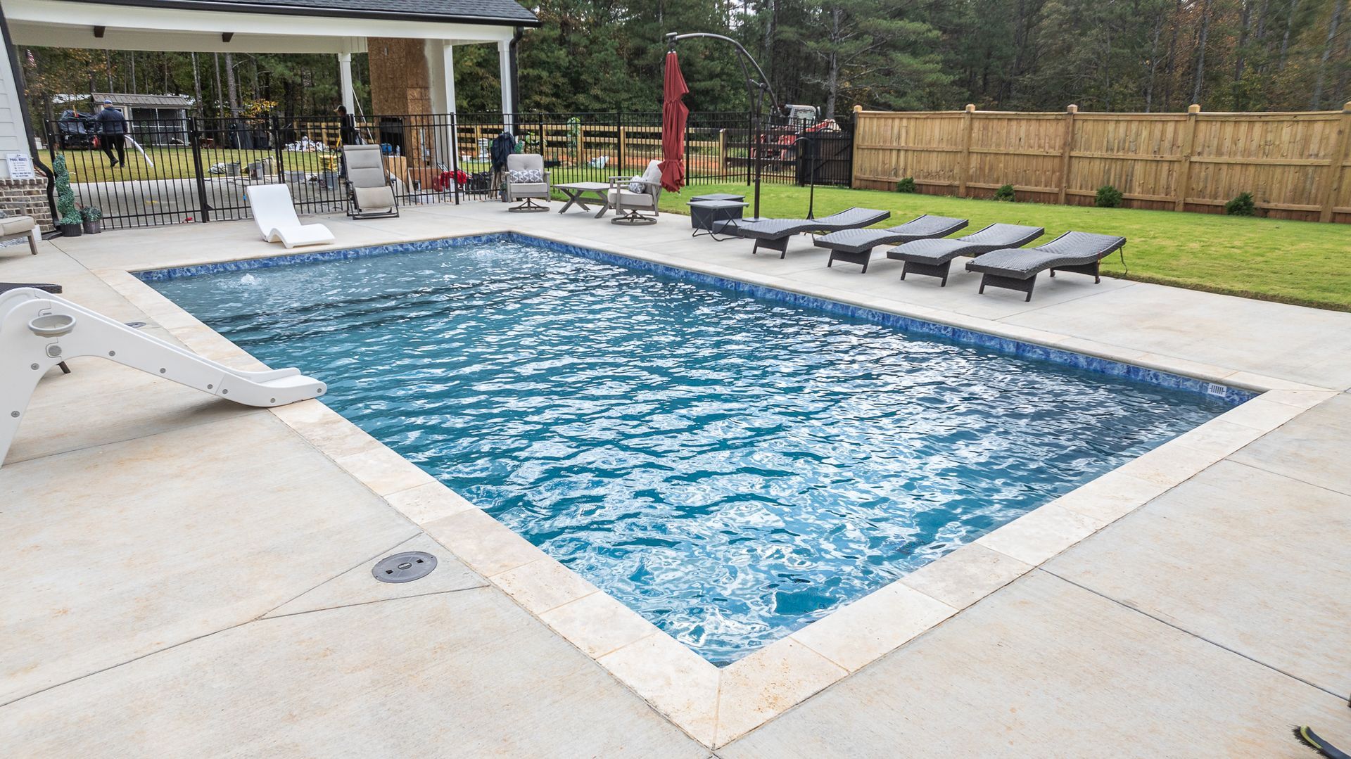 A large swimming pool surrounded by chairs and umbrellas in a backyard.