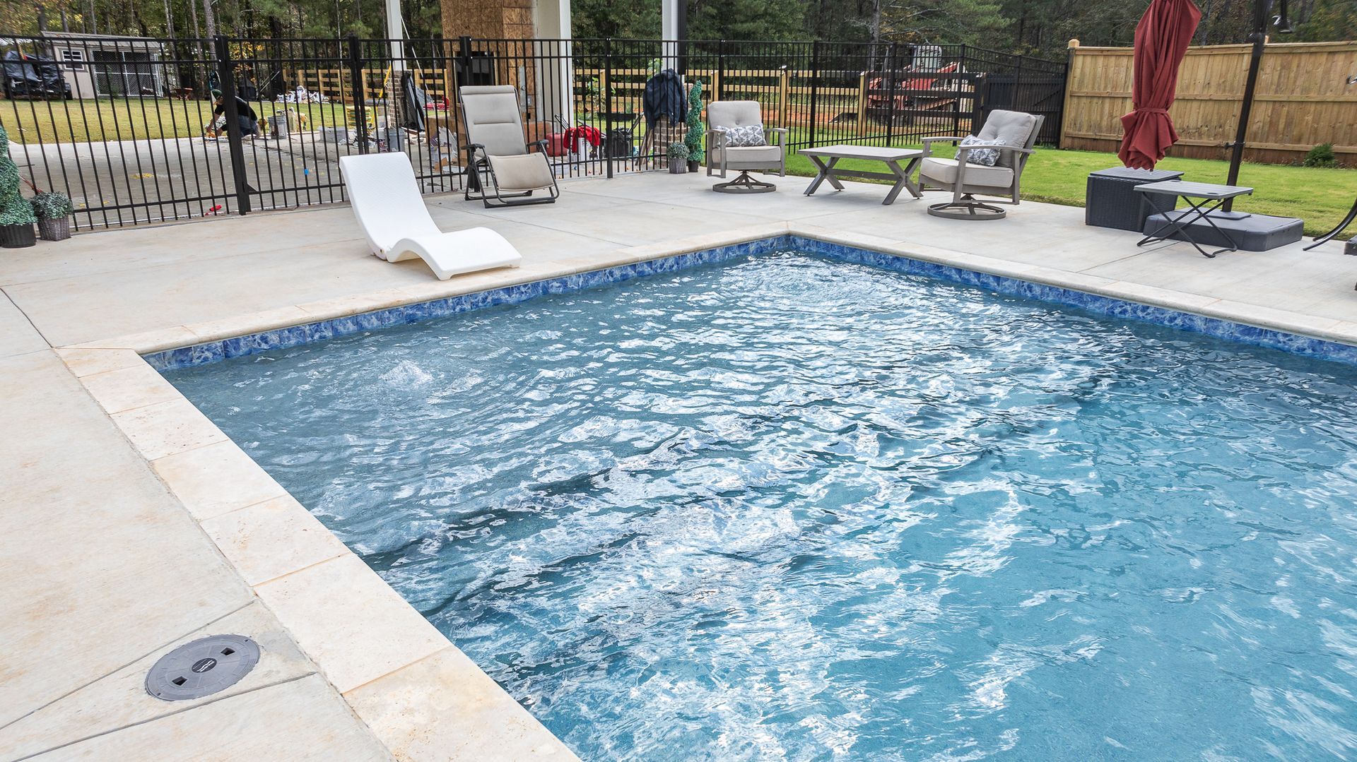 A large swimming pool surrounded by chairs and umbrellas in a backyard.