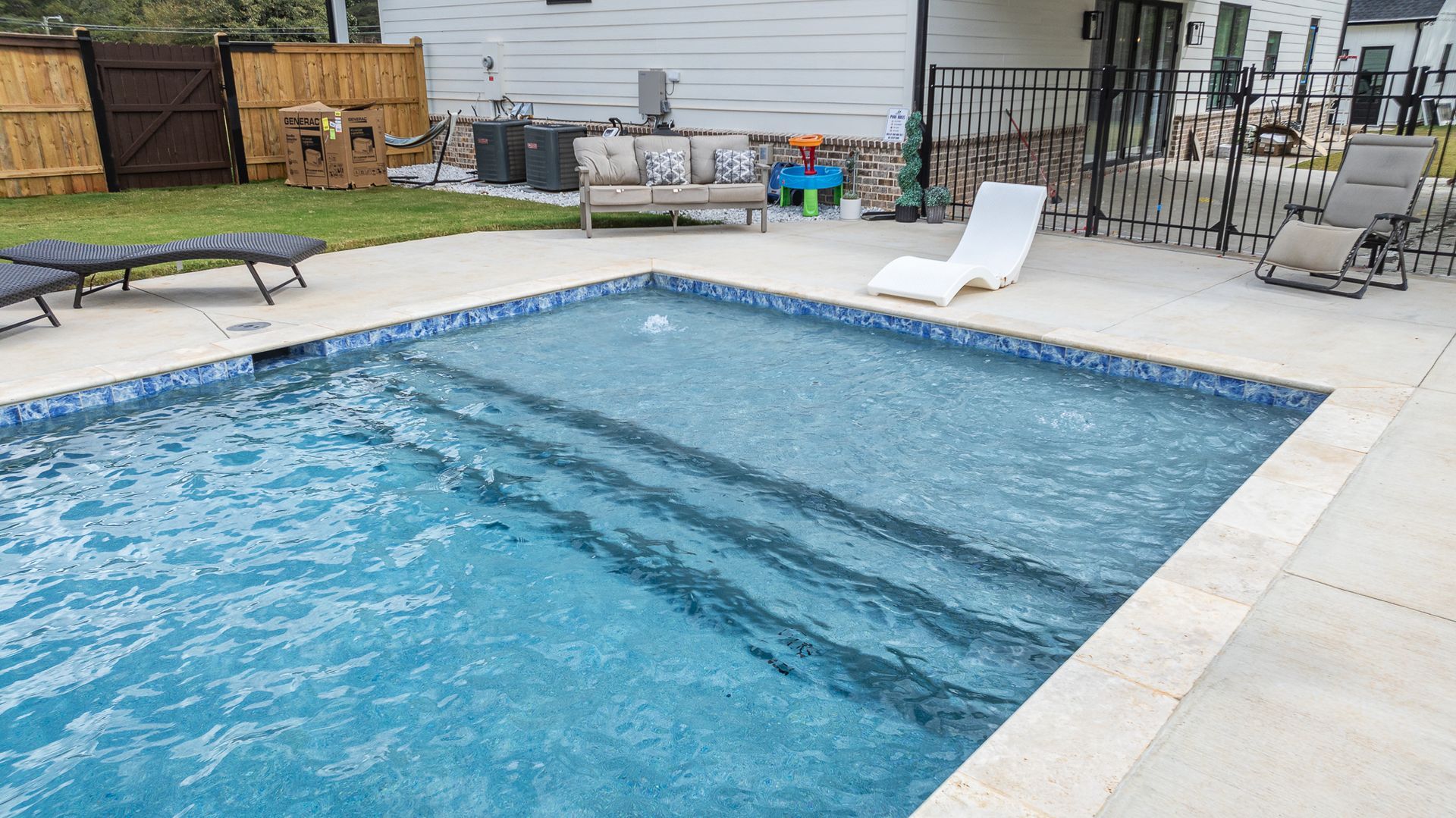A large swimming pool with stairs and chairs in a backyard.