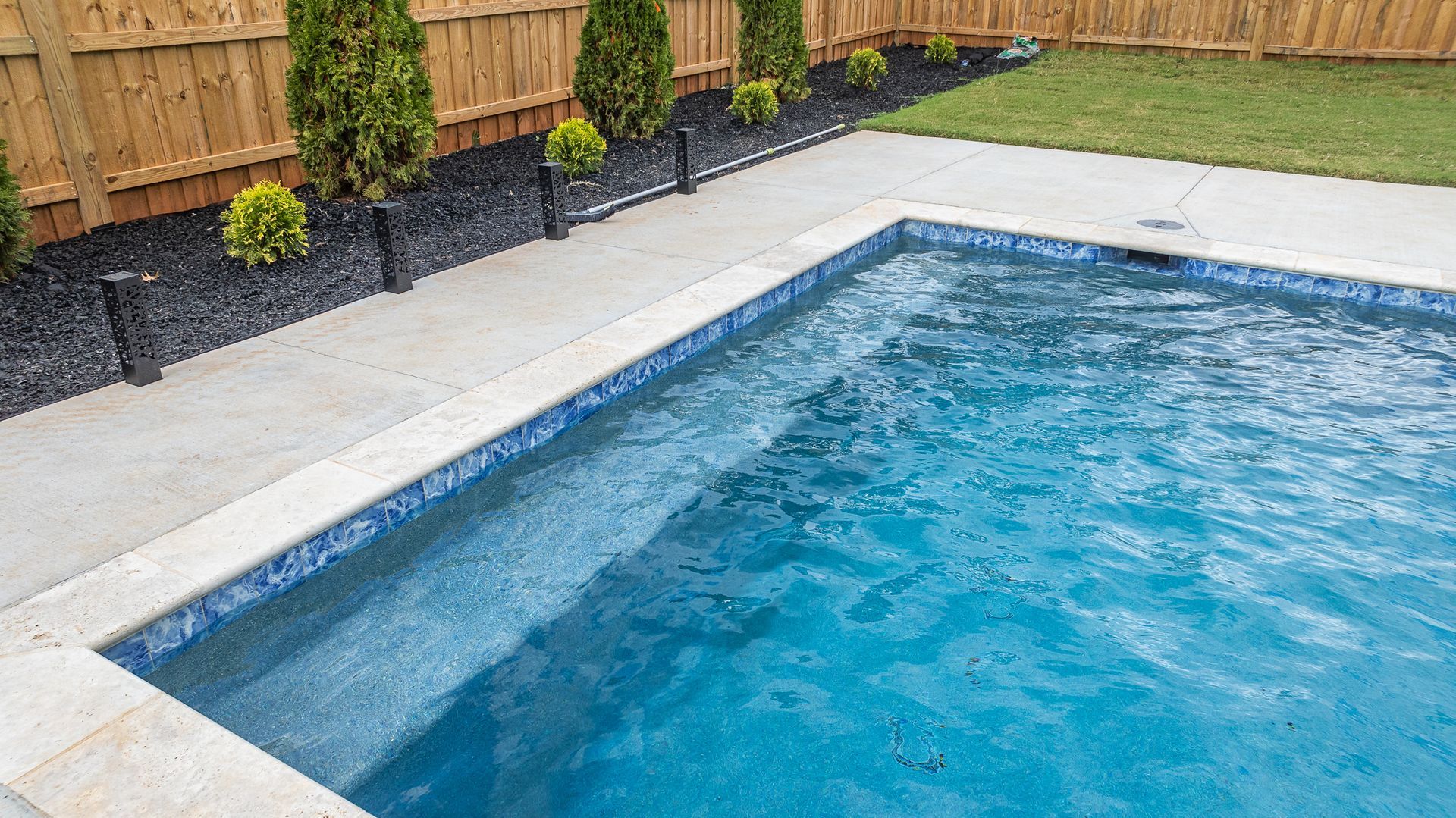 A large swimming pool in a backyard with a wooden fence surrounding it.
