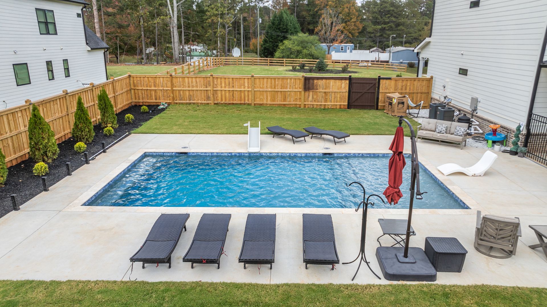 There is a large swimming pool in the backyard with chairs and umbrellas.