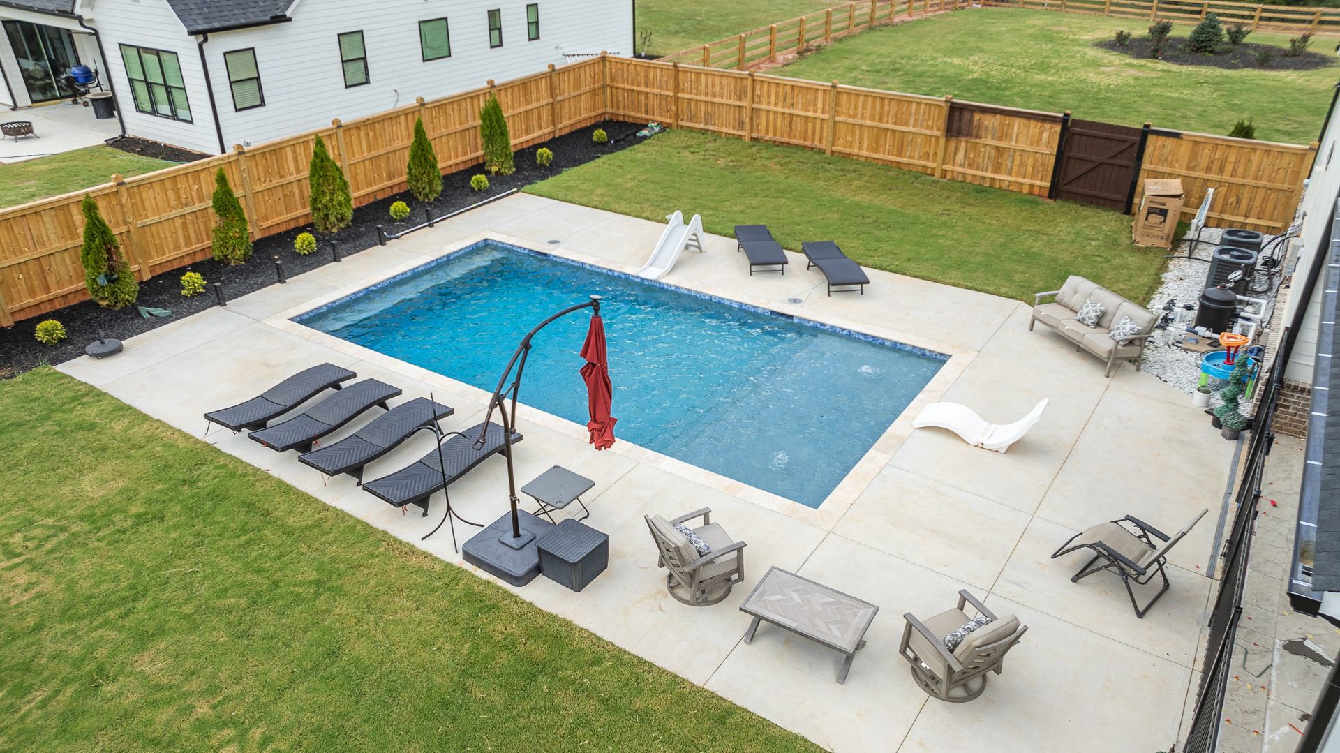 An aerial view of a large swimming pool surrounded by chairs and umbrellas in a backyard.