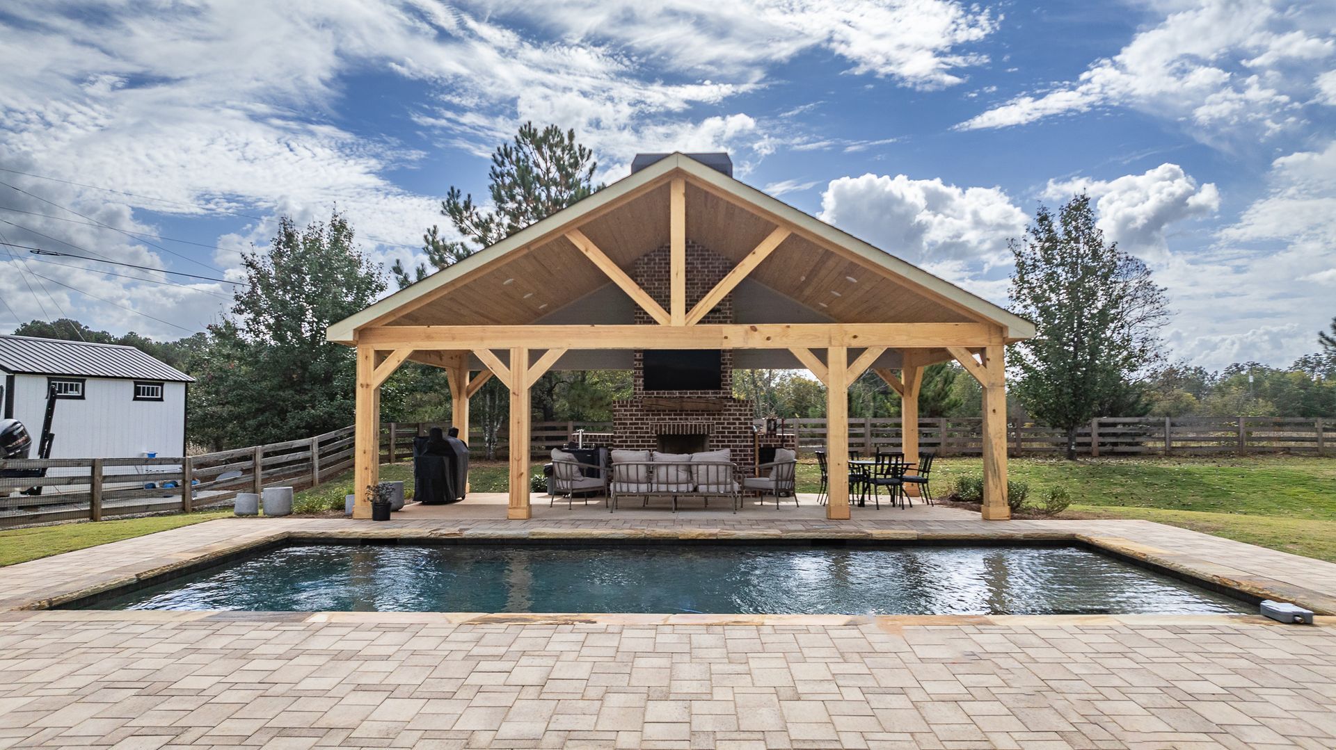 There is a large swimming pool under a wooden pavilion.
