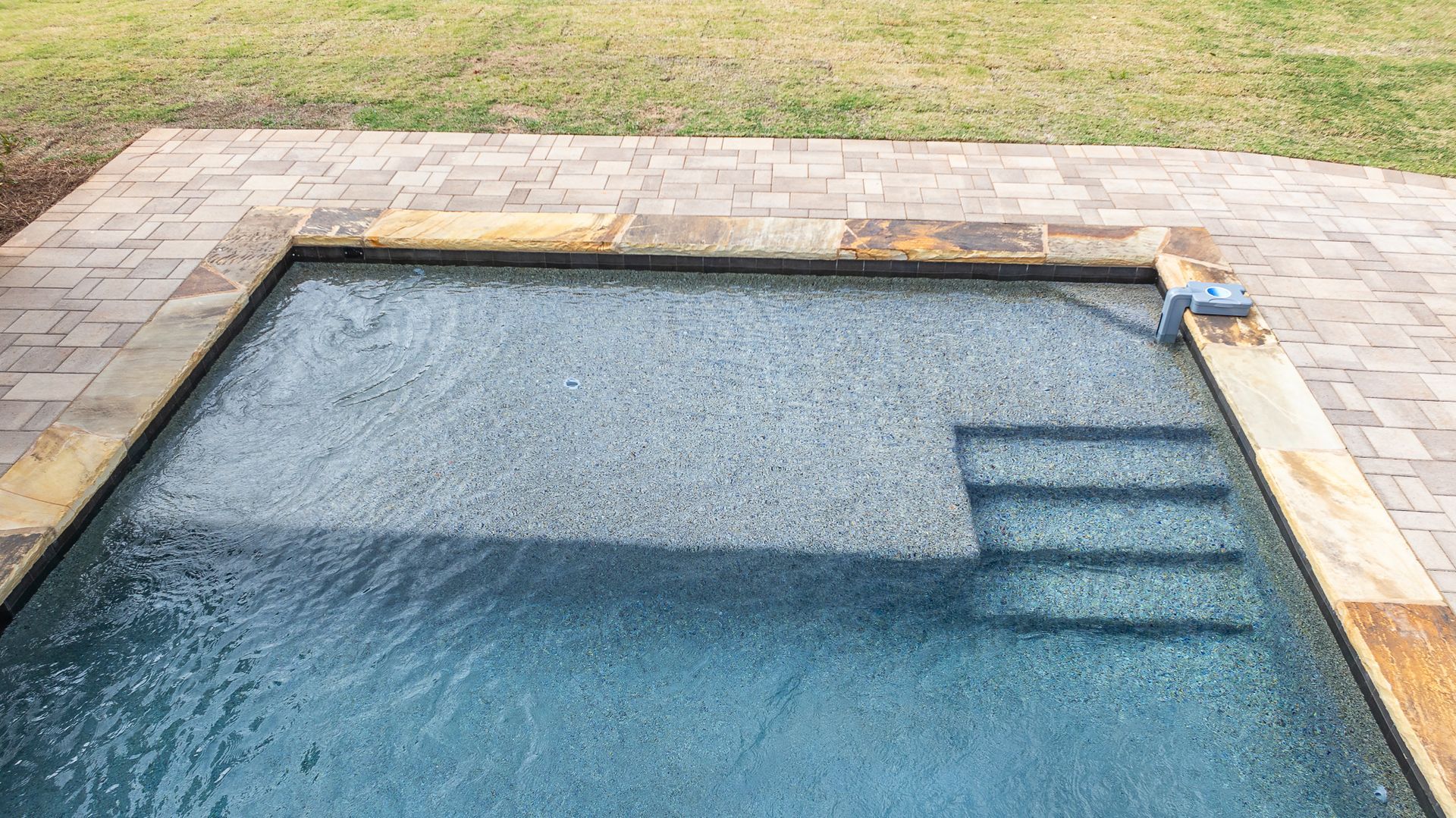 A swimming pool with stairs leading to it is sitting on top of a brick patio.