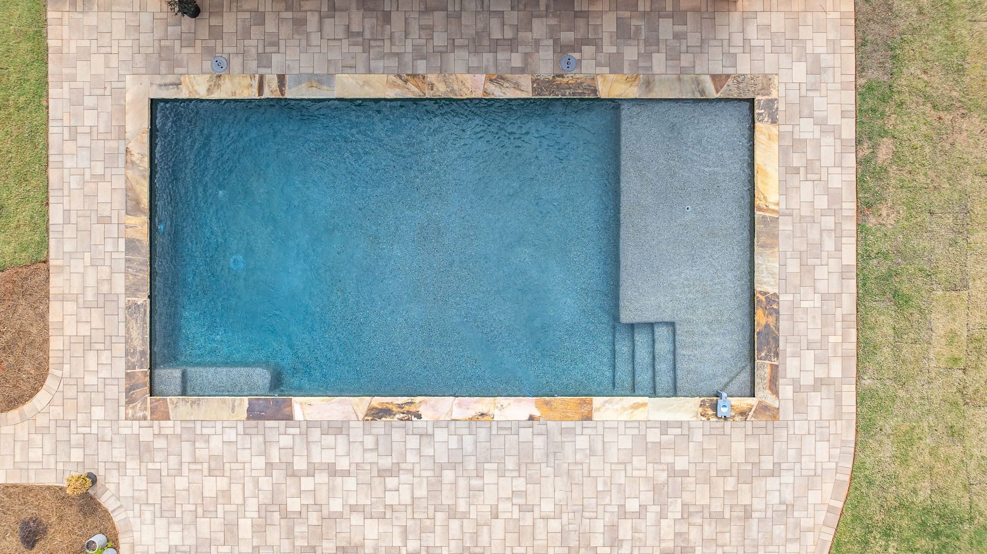 An aerial view of a swimming pool surrounded by bricks and grass.