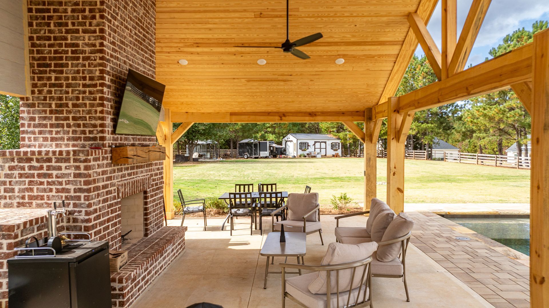 A patio with a fireplace , chairs , a table and a ceiling fan.