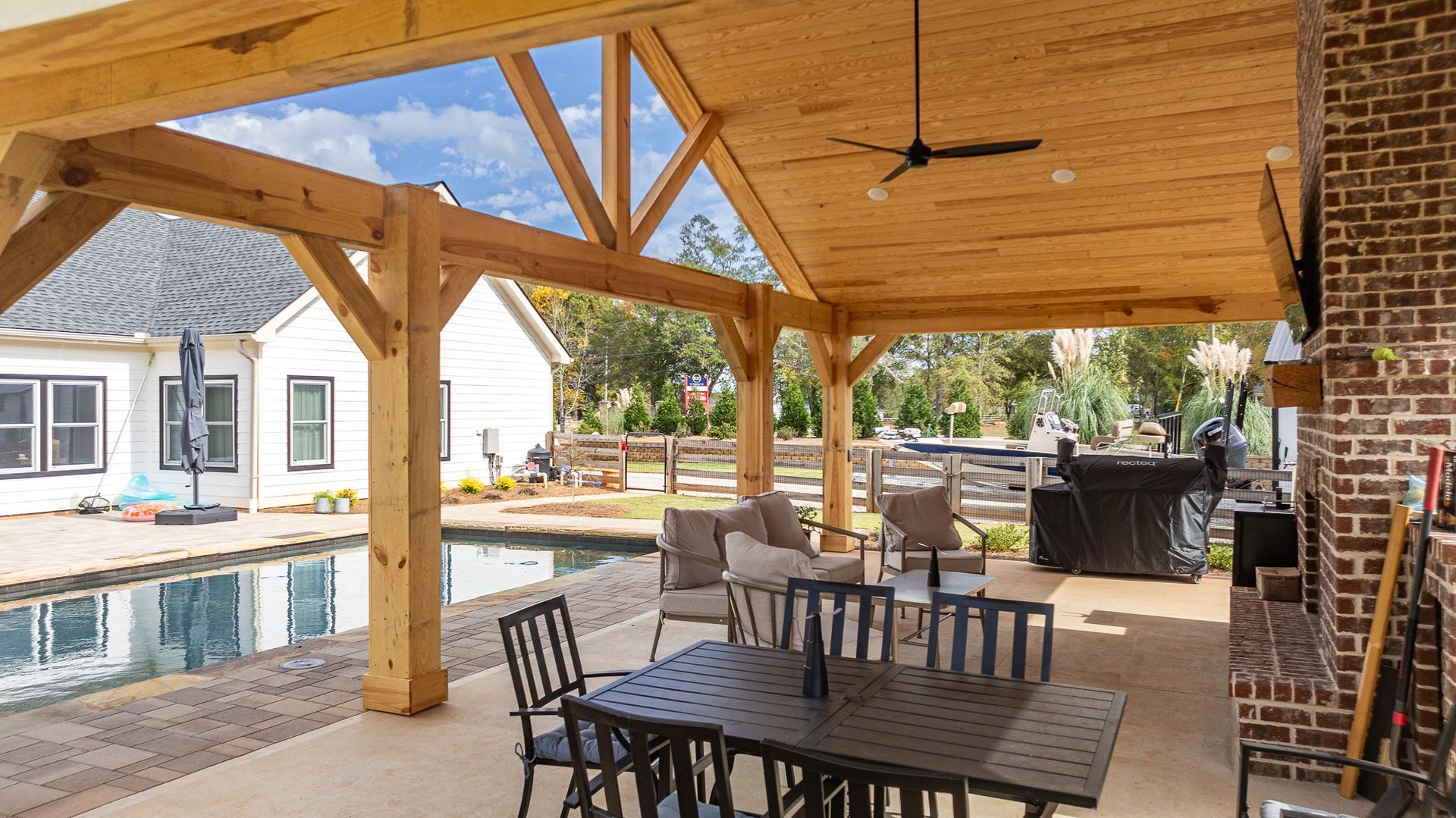 A patio with a table and chairs under a wooden roof.